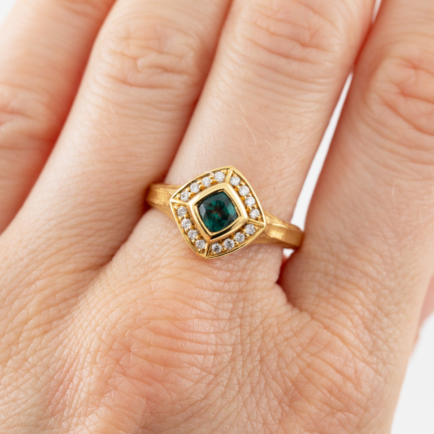 Gold ring with a green Alexandrite gemstone and diamond accents on a hand