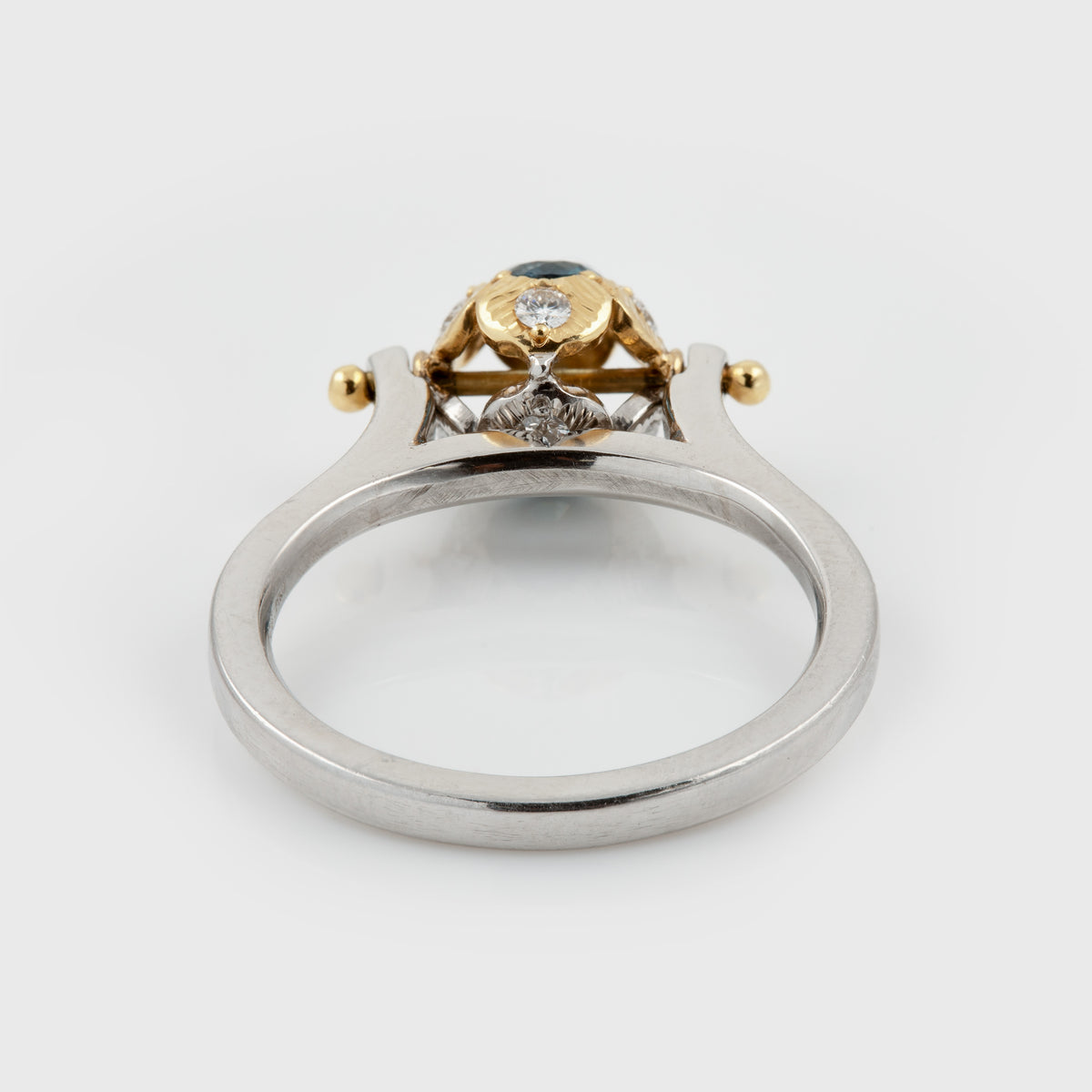 Back view of Platinum two-tone ring featuring a round blue sapphire center stone surrounded by small diamonds, with a polished silver-colored band and gold accents. Photographed on a white background. 