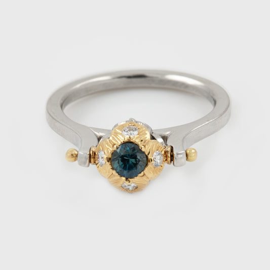 Platinum two-tone ring featuring a round blue sapphire center stone set in gold surrounded  by small diamonds, with a polished silver-colored band and gold accents. Photographed on a white background. 