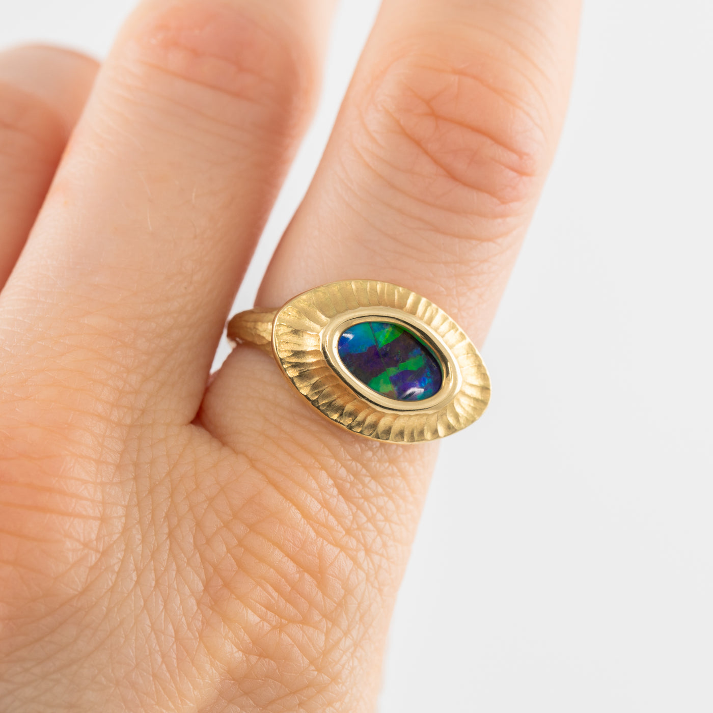 Gold ring with a colorful gemstone on a finger against a white background