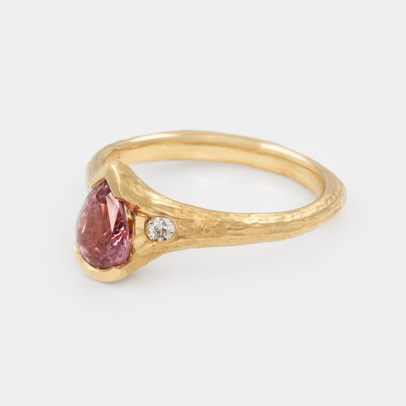 Gold ring with a pink gemstone and small diamond on a light gray background