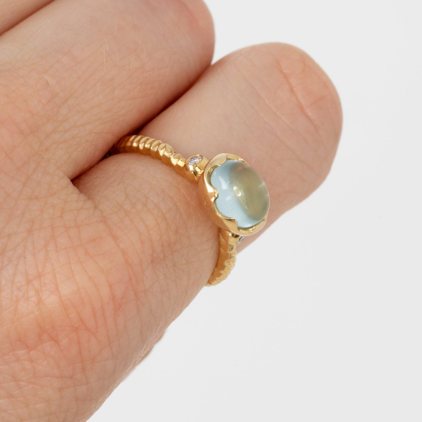 Gold ring with a light blue gemstone on a finger against a white background