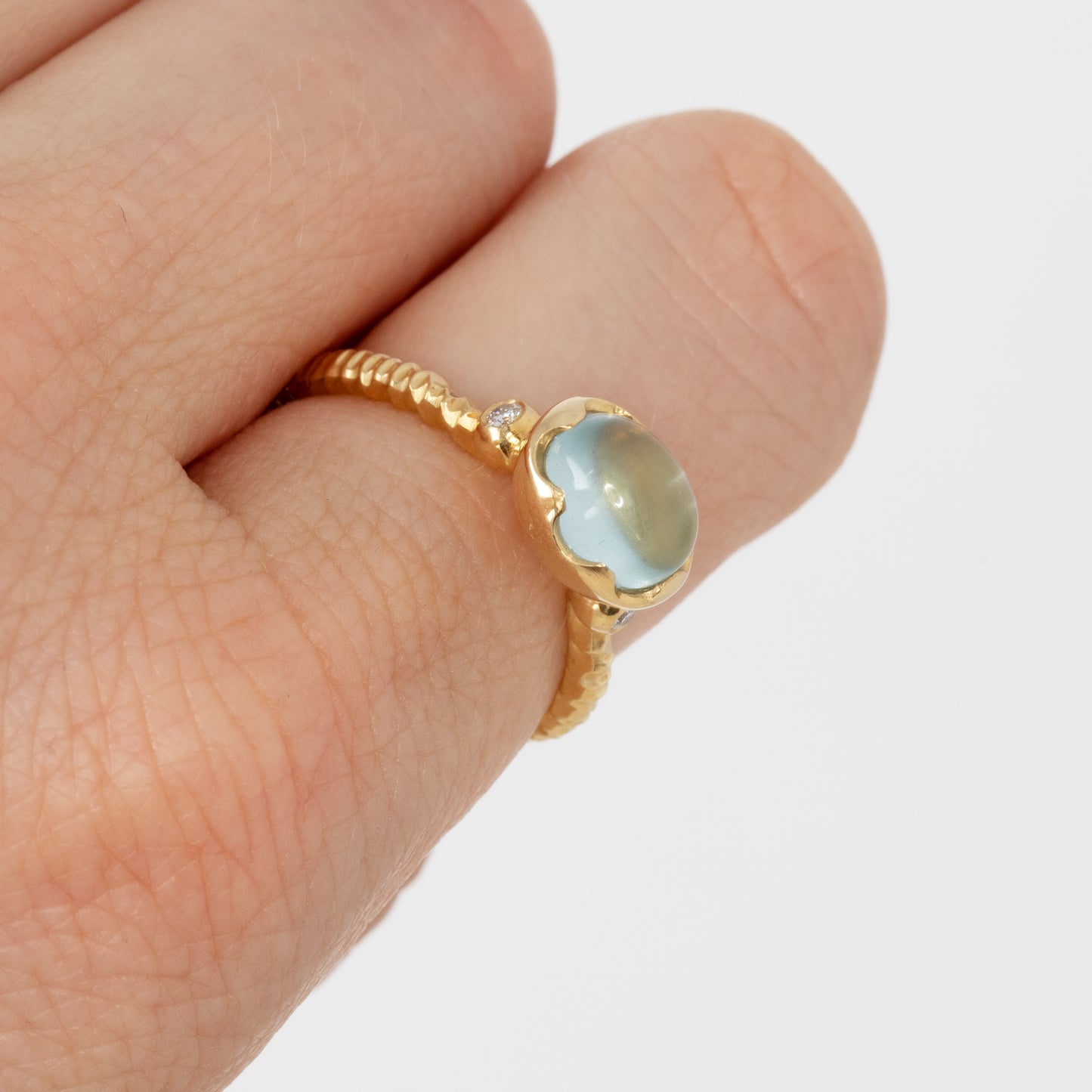 Gold ring with a light blue gemstone on a finger against a white background