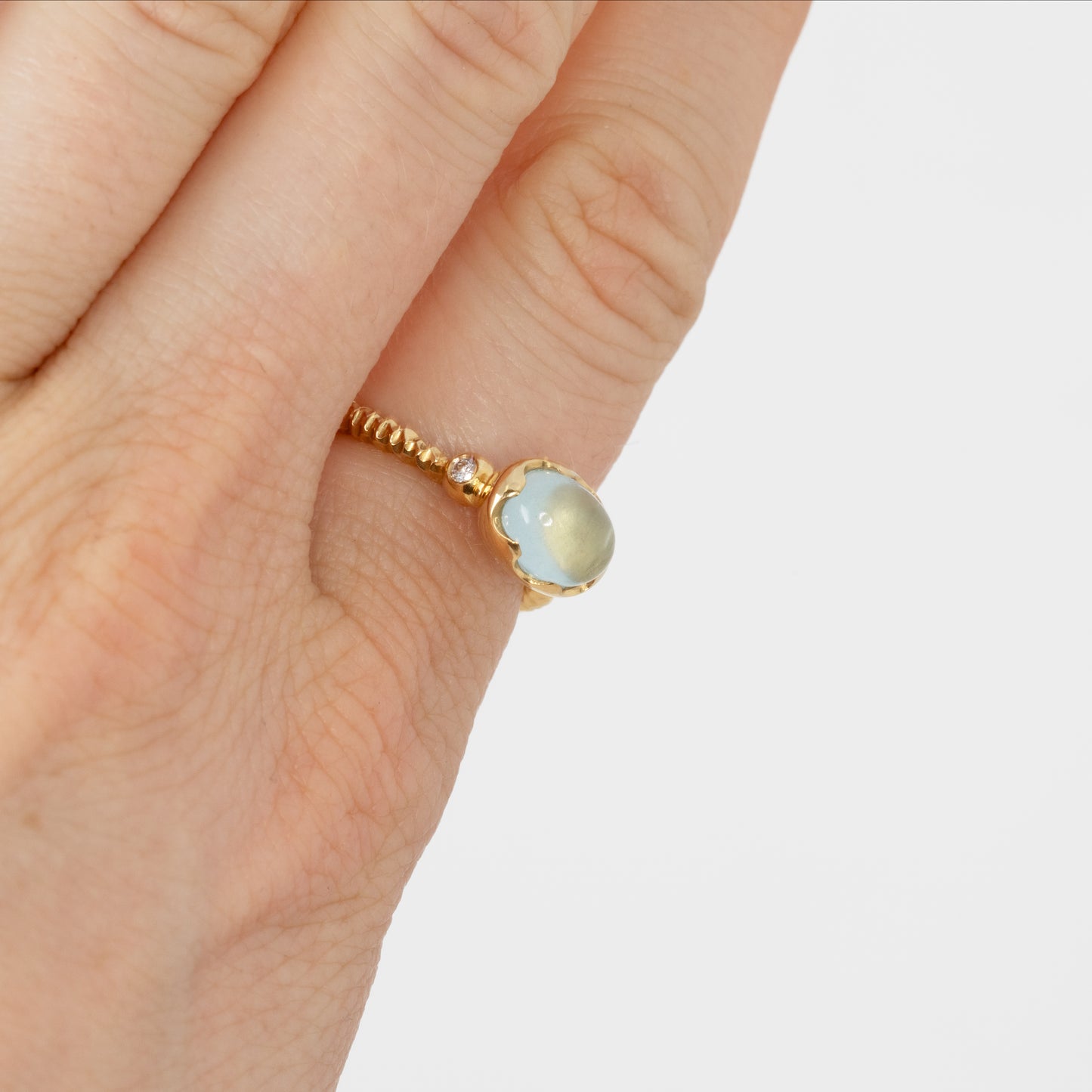 Gold ring with a light blue gemstone on a hand against a white background