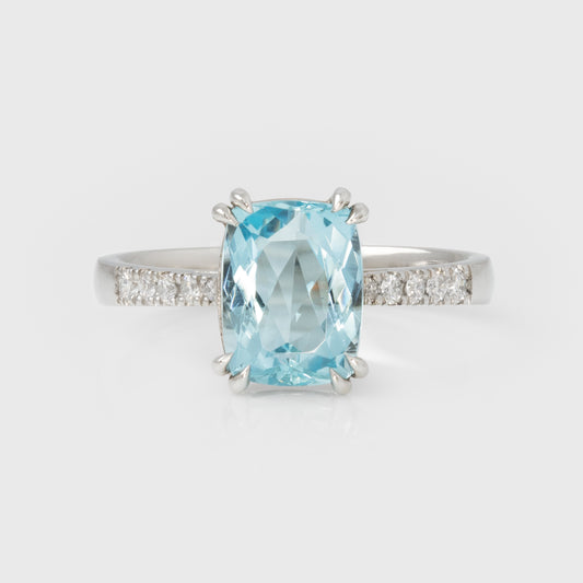 Silver ring with a large blue gemstone and smaller diamonds on a light gray background