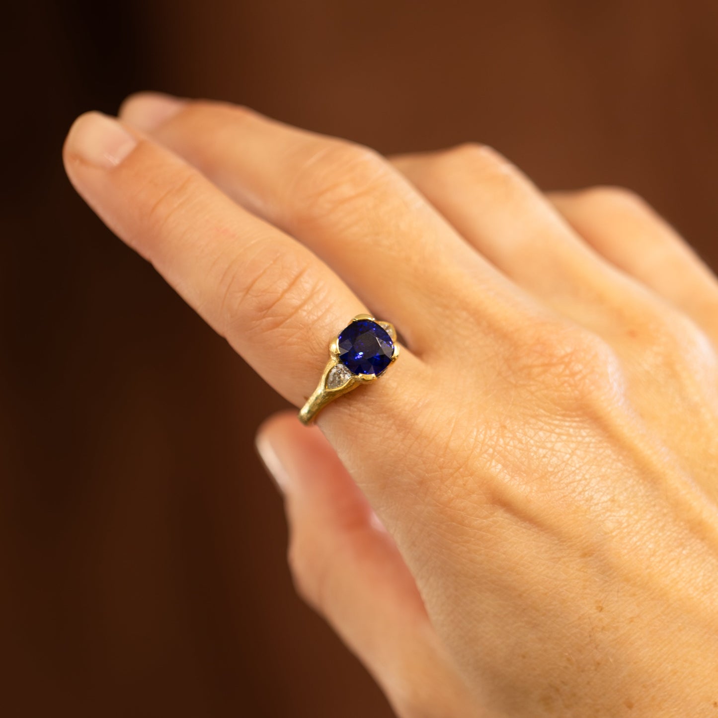 Hand wearing a gold ring with a blue gemstone on a blurred background