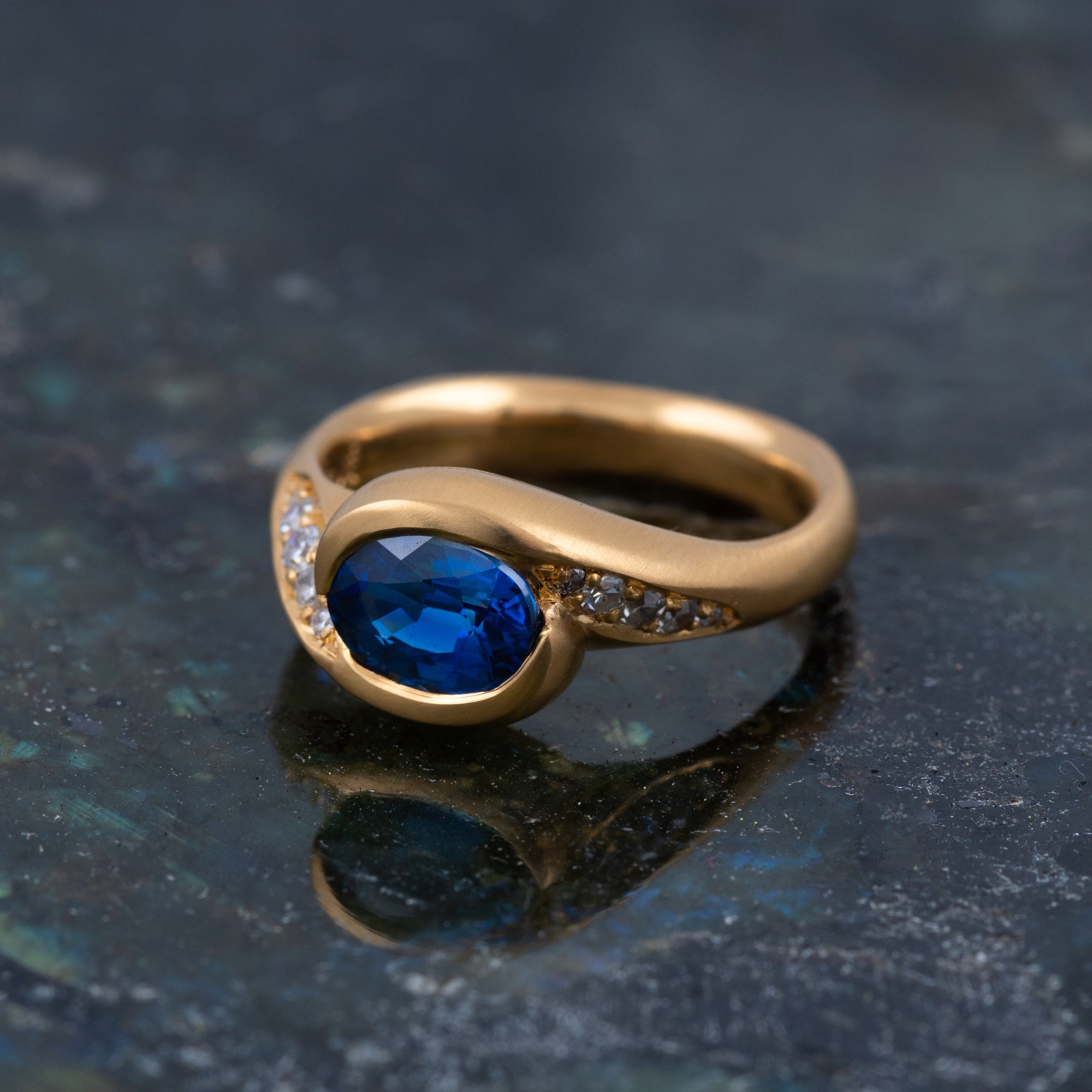 Gold ring with blue gemstone and accent gemstones on a textured background