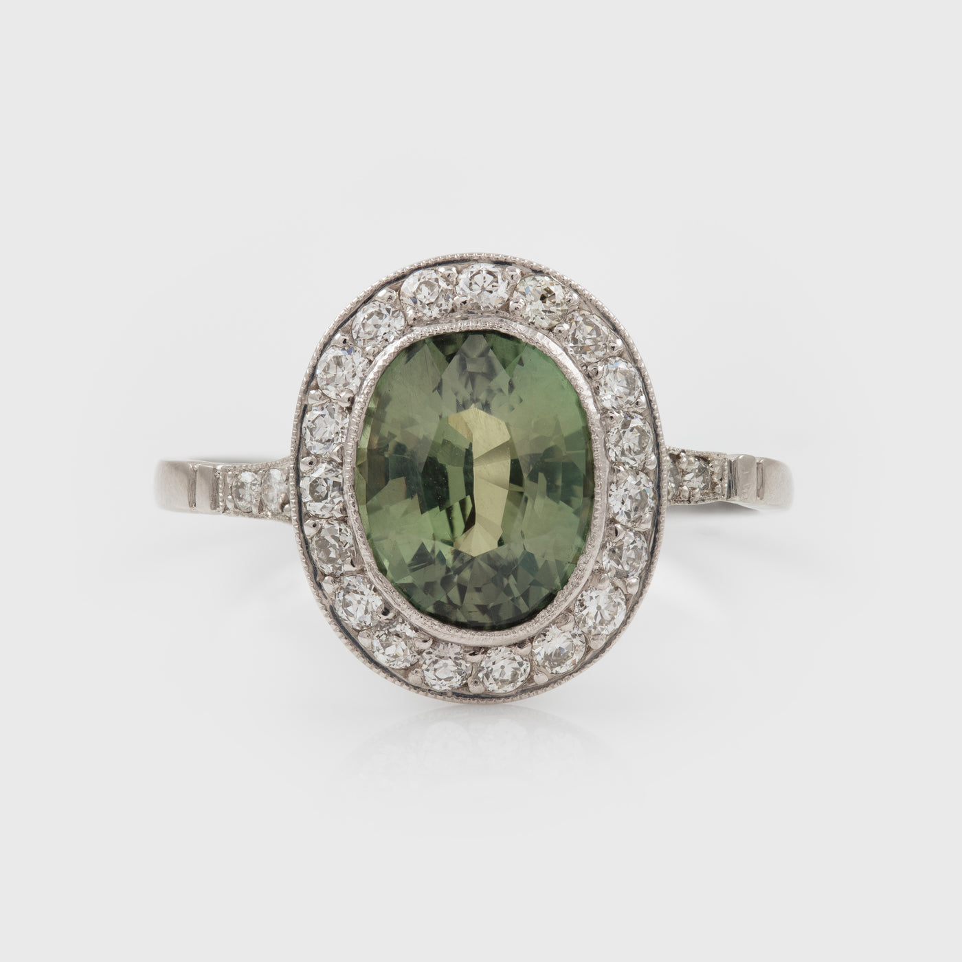 Platinum ring with a green Alexandrite gemstone and diamond accents on a white background