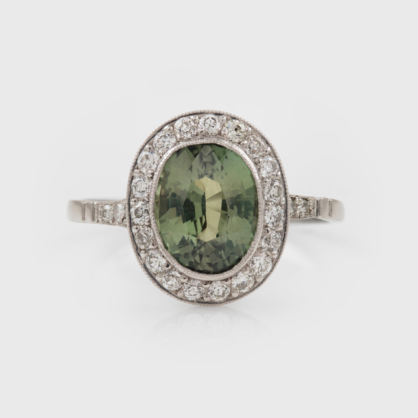 Platinum ring with a green Alexandrite gemstone and diamond accents on a white background
