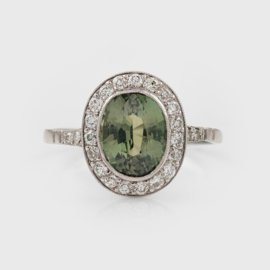 Platinum ring with a green Alexandrite gemstone and diamond accents on a white background