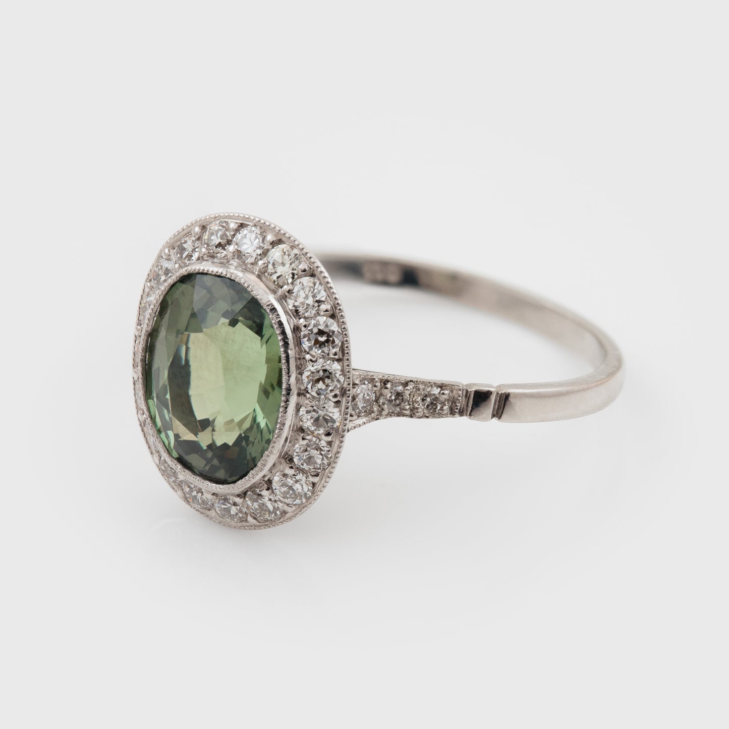 Platinum ring with a green Alexandrite gemstone and diamond accents on a white background