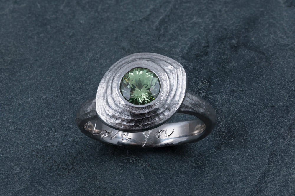 Silver ring with a green gemstone on a dark gray surface