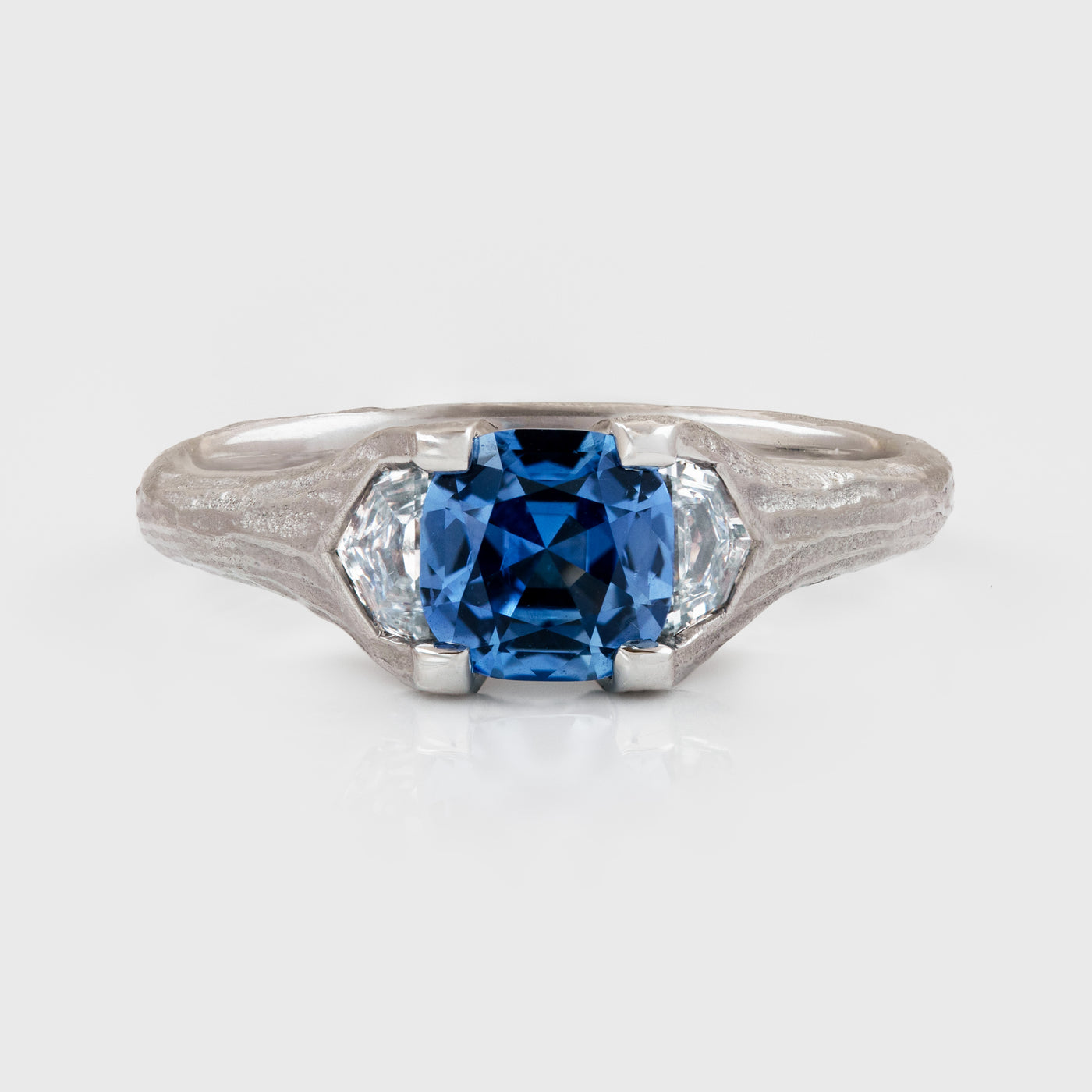 Platinum ring featuring cushion faceted blue Sapphire flanked by epaulette Diamonds