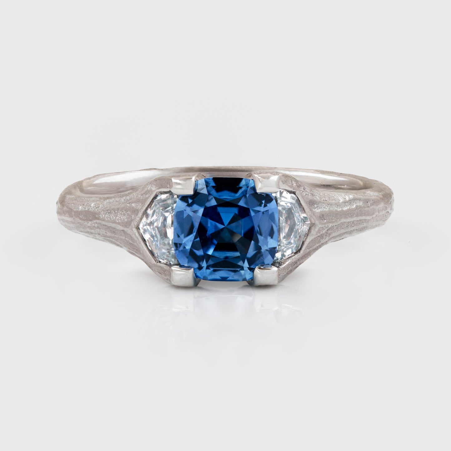 Platinum ring featuring cushion faceted blue Sapphire flanked by epaulette Diamonds