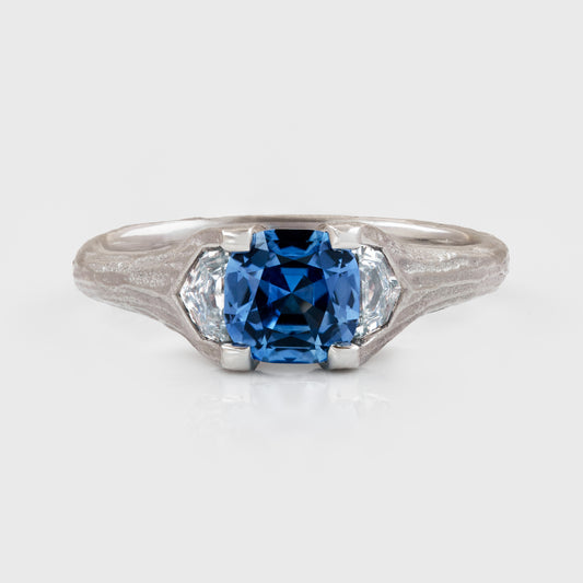 Platinum ring featuring cushion faceted blue Sapphire flanked by epaulette Diamonds