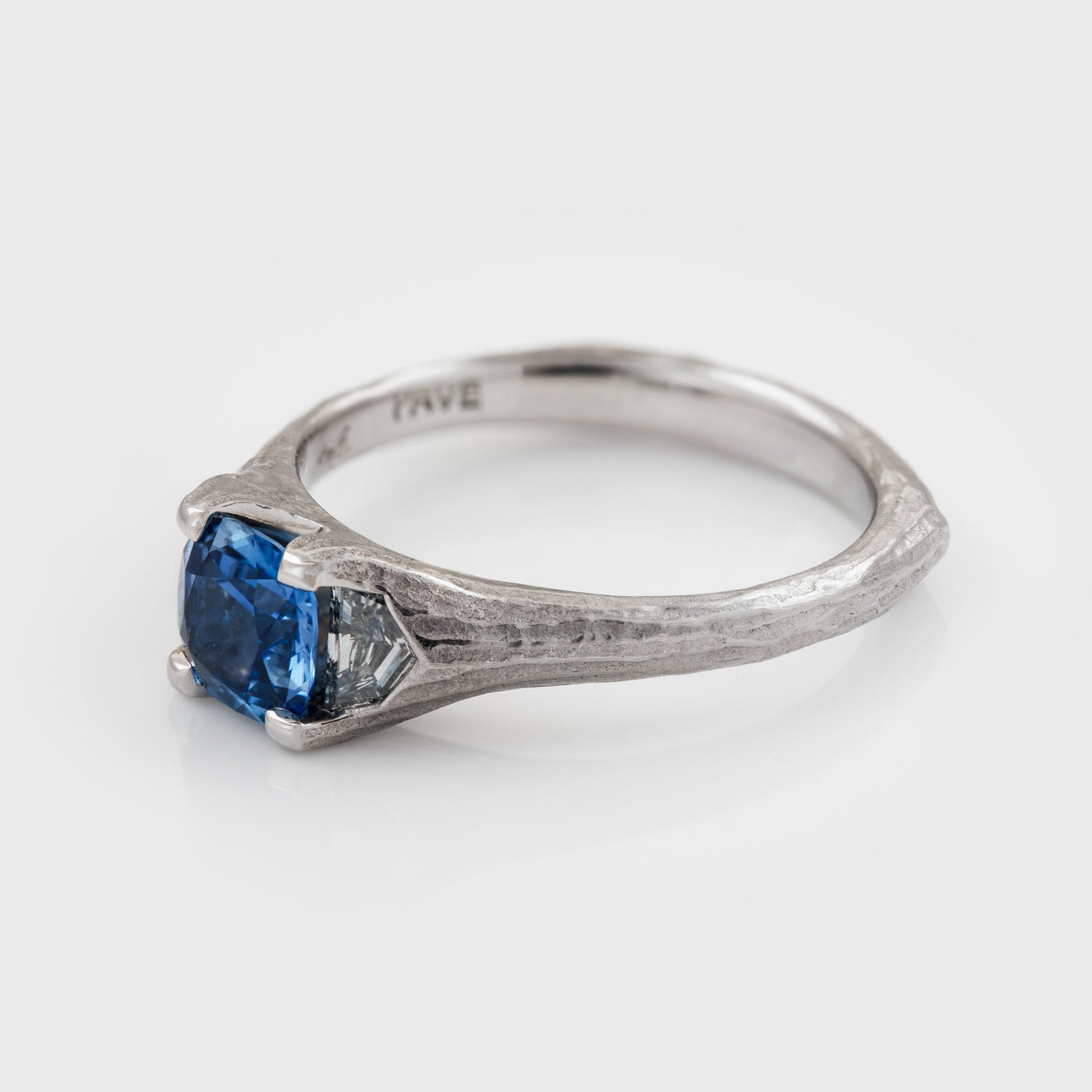 Side view of platinum ring featuring cushion faceted blue Sapphire flanked by epaulette Diamonds