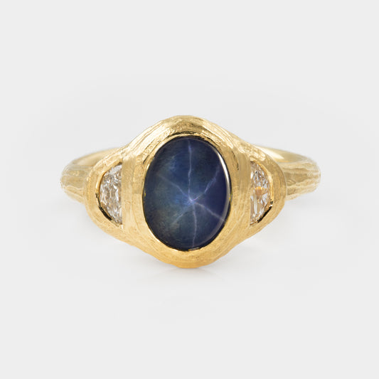 Gold ring with blue star sapphire and side diamonds on white background