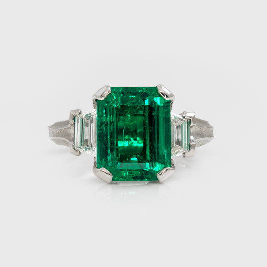 Emerald ring with diamond accents on a white background