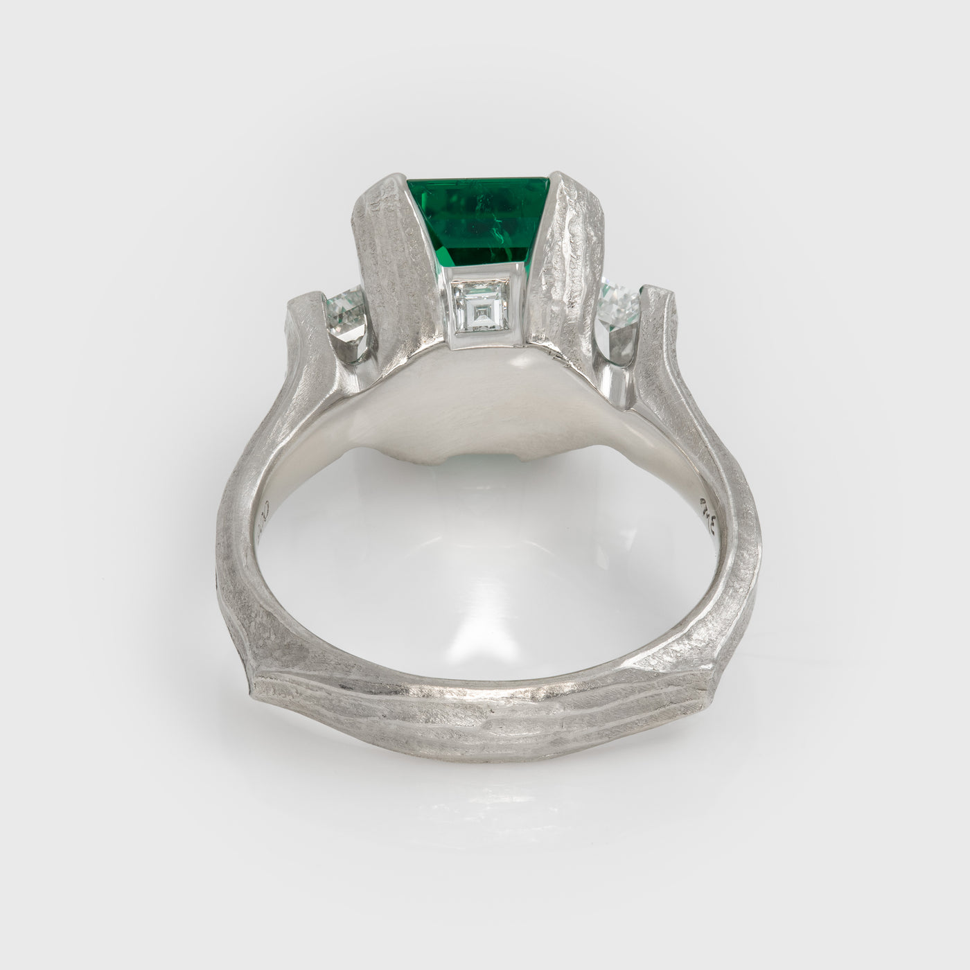 Platinum ring with a green gemstone on a white background