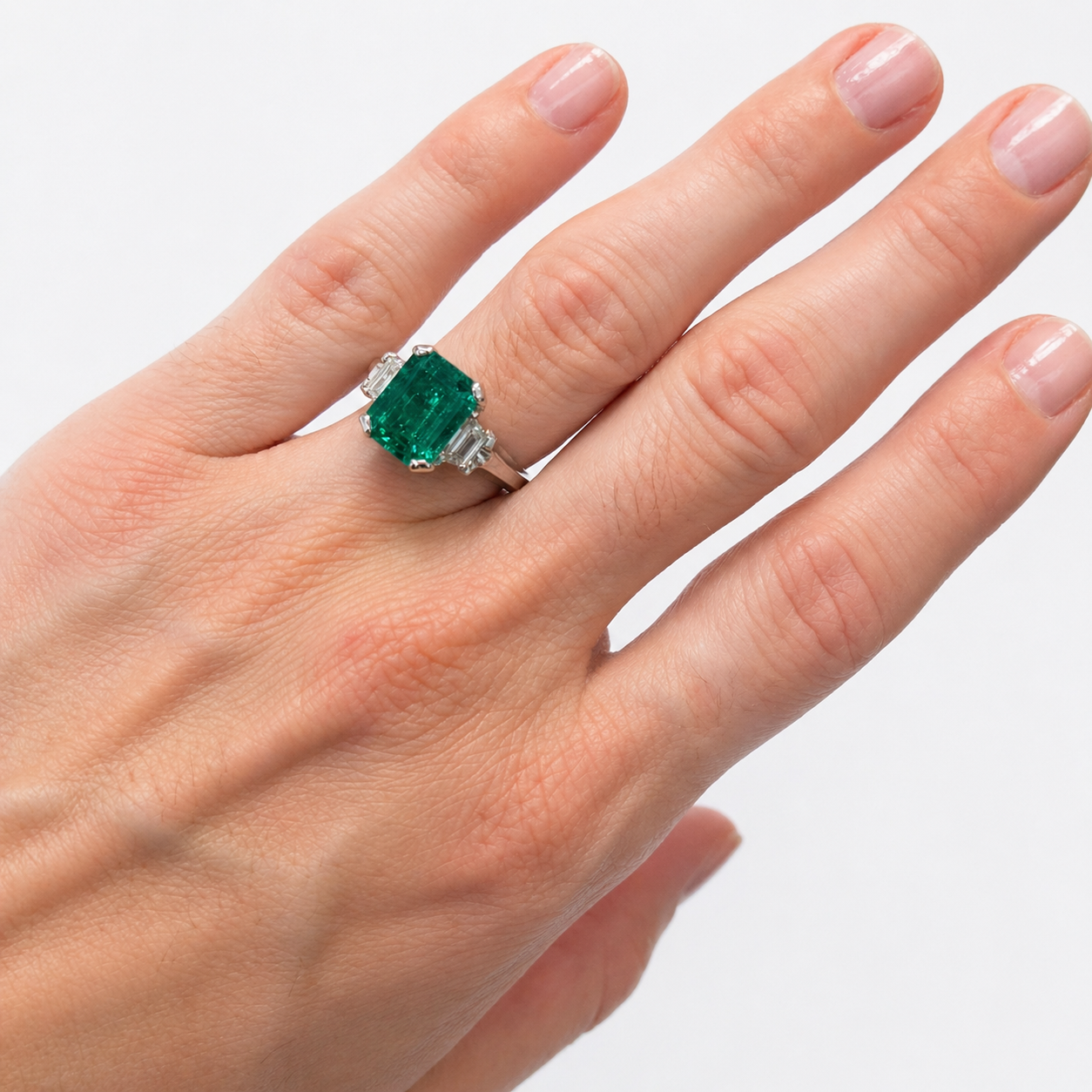 Emerald ring with diamond accepts on a hand against a white background