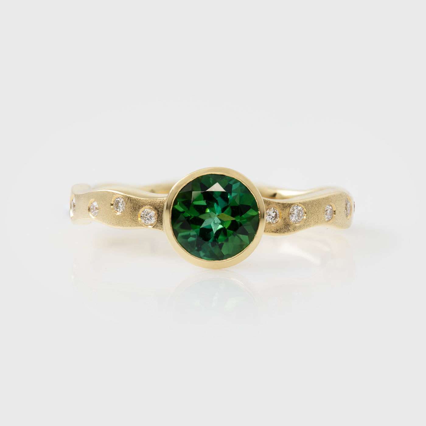 Gold ring with a green gemstone and smaller diamonds on a white background