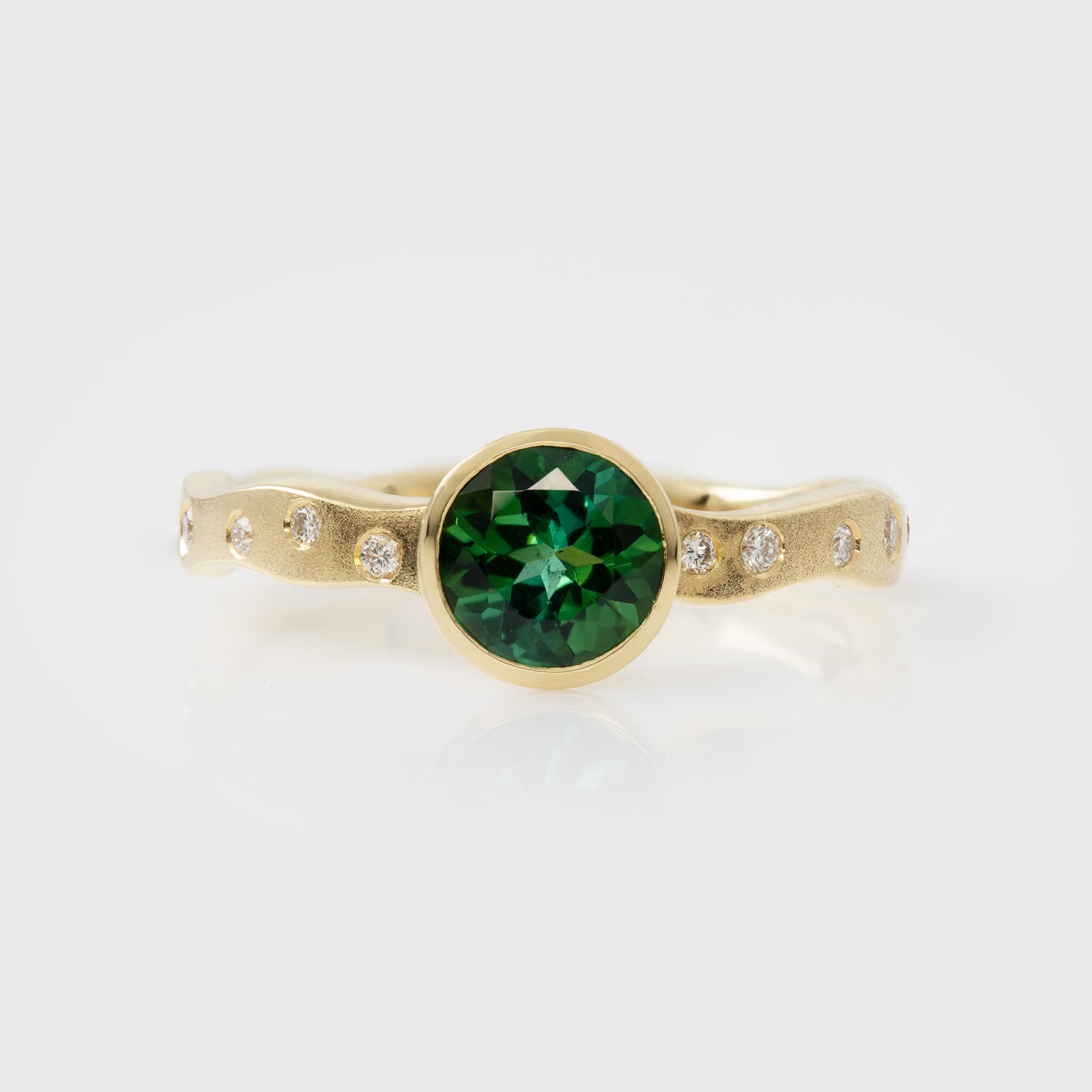 Gold ring with a green gemstone and smaller diamonds on a white background
