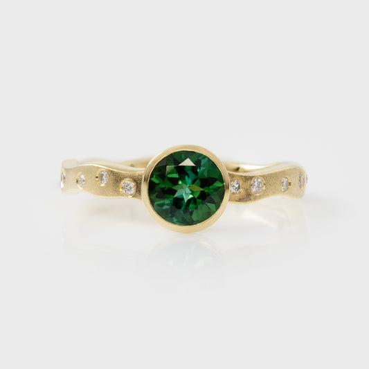 Gold ring with a green gemstone and smaller diamonds on a white background