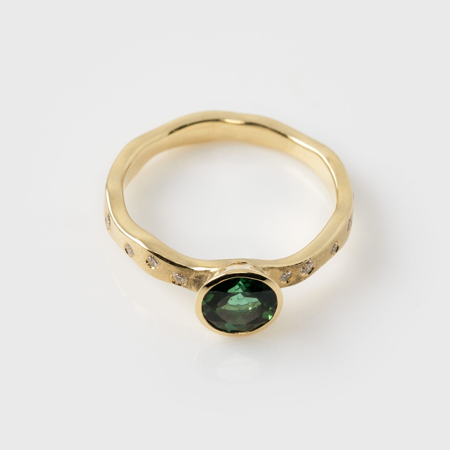 Gold ring with a green gemstone on a white background from above