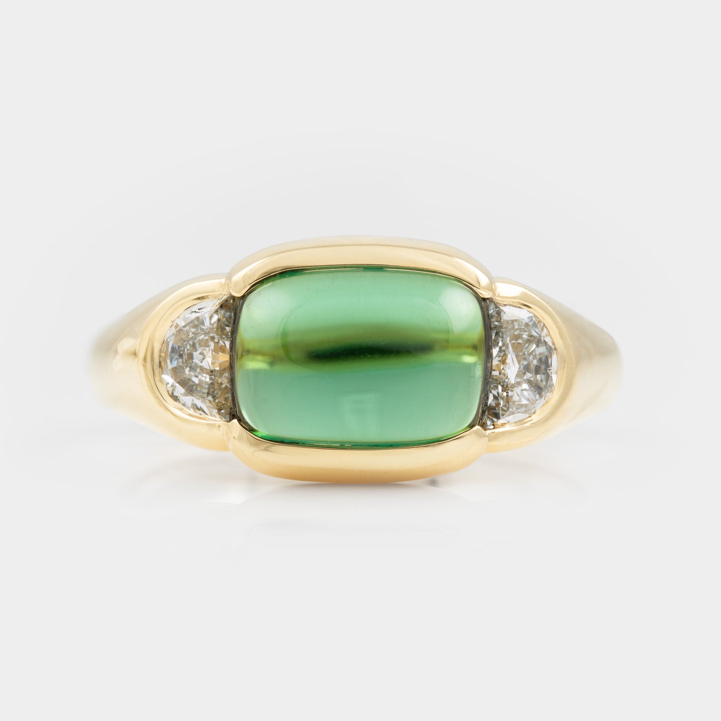 Gold ring with a green gemstone and two smaller diamonds on a white background