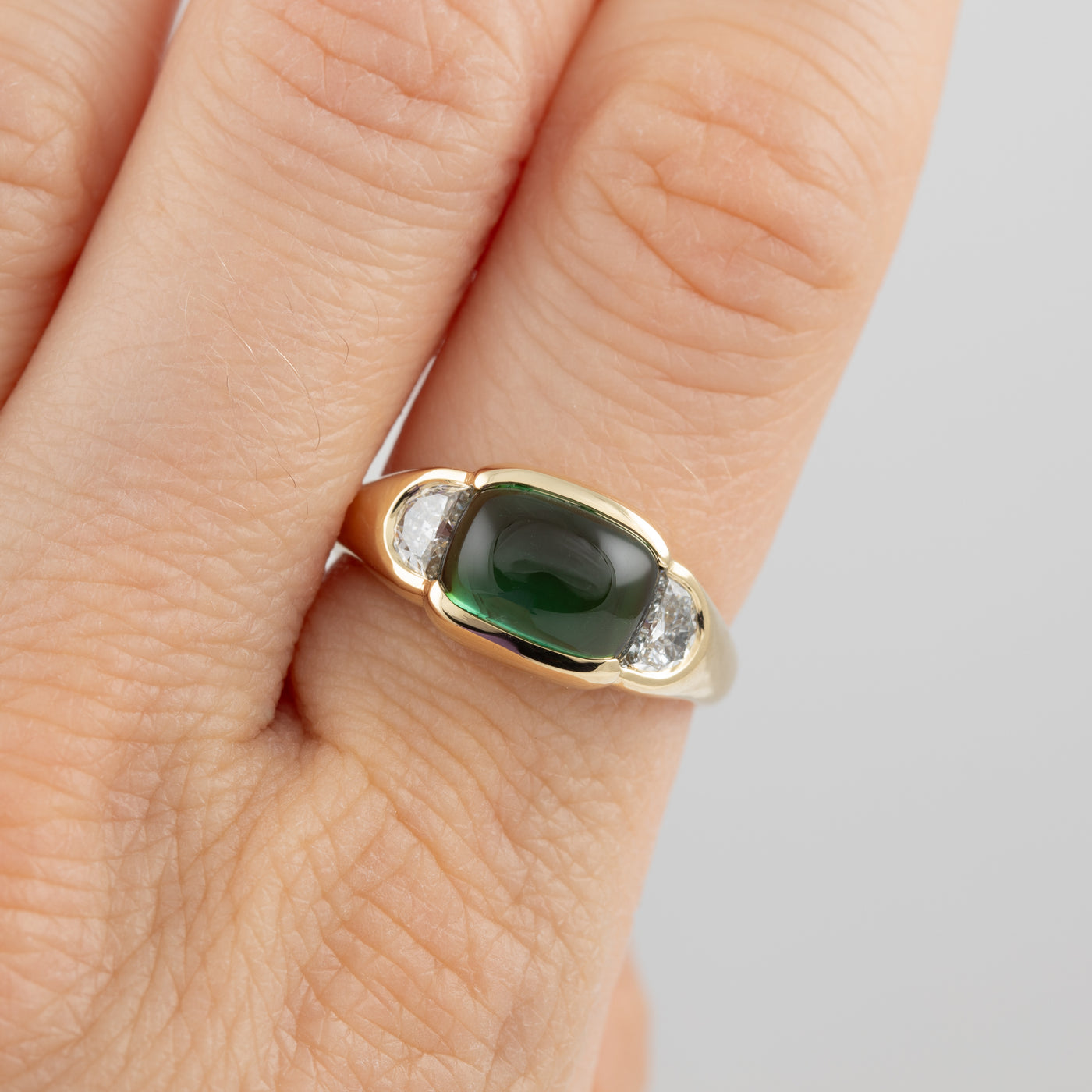 Gold ring with a green gemstone on a person's finger against a neutral background