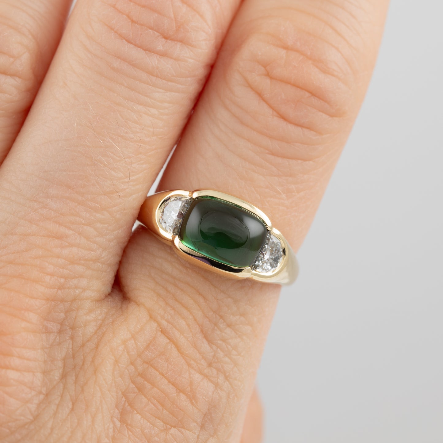 Gold ring with a green gemstone on a person's finger against a neutral background