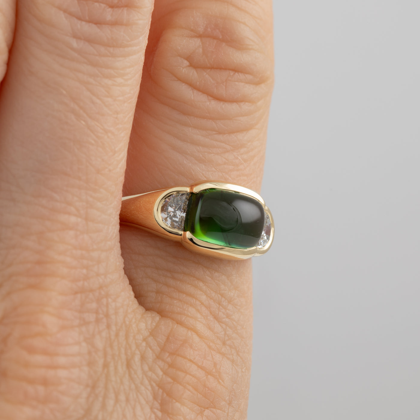Gold ring with a green gemstone on a finger against a neutral background