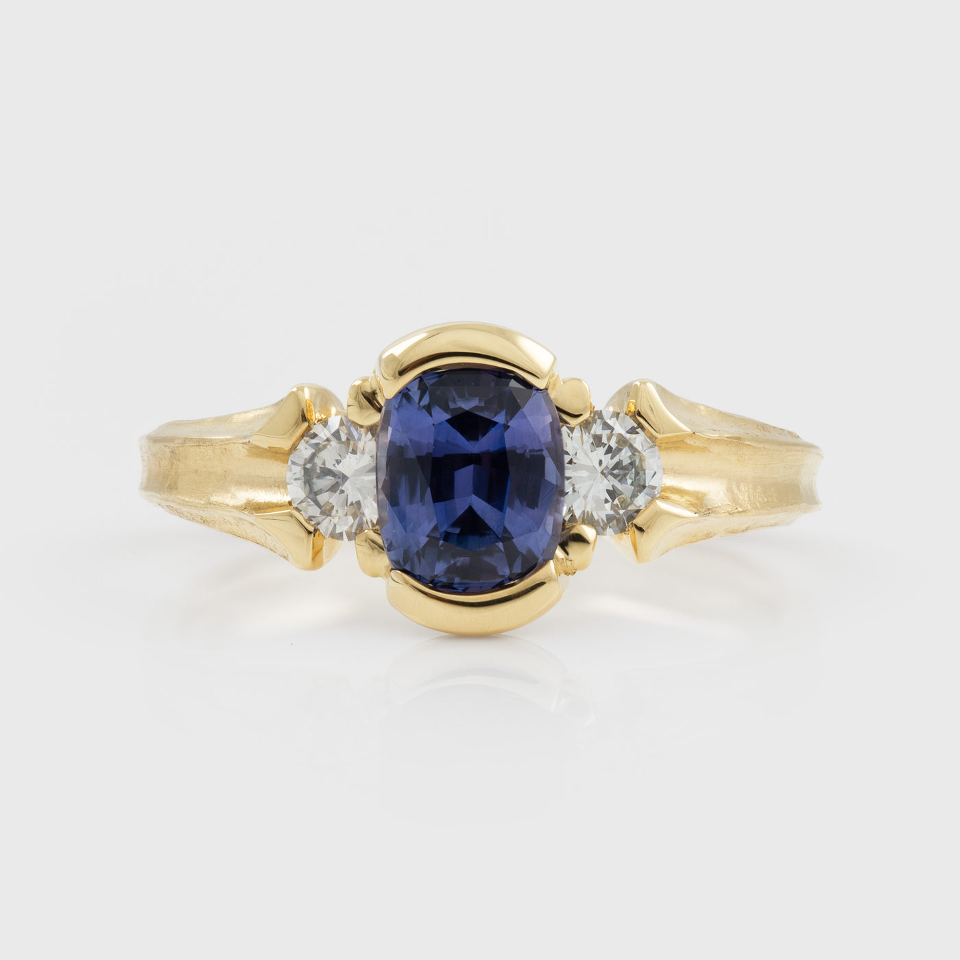 Yellow gold ring featuring half bezel set oval purple Sapphire flanked by round white Diamond accents