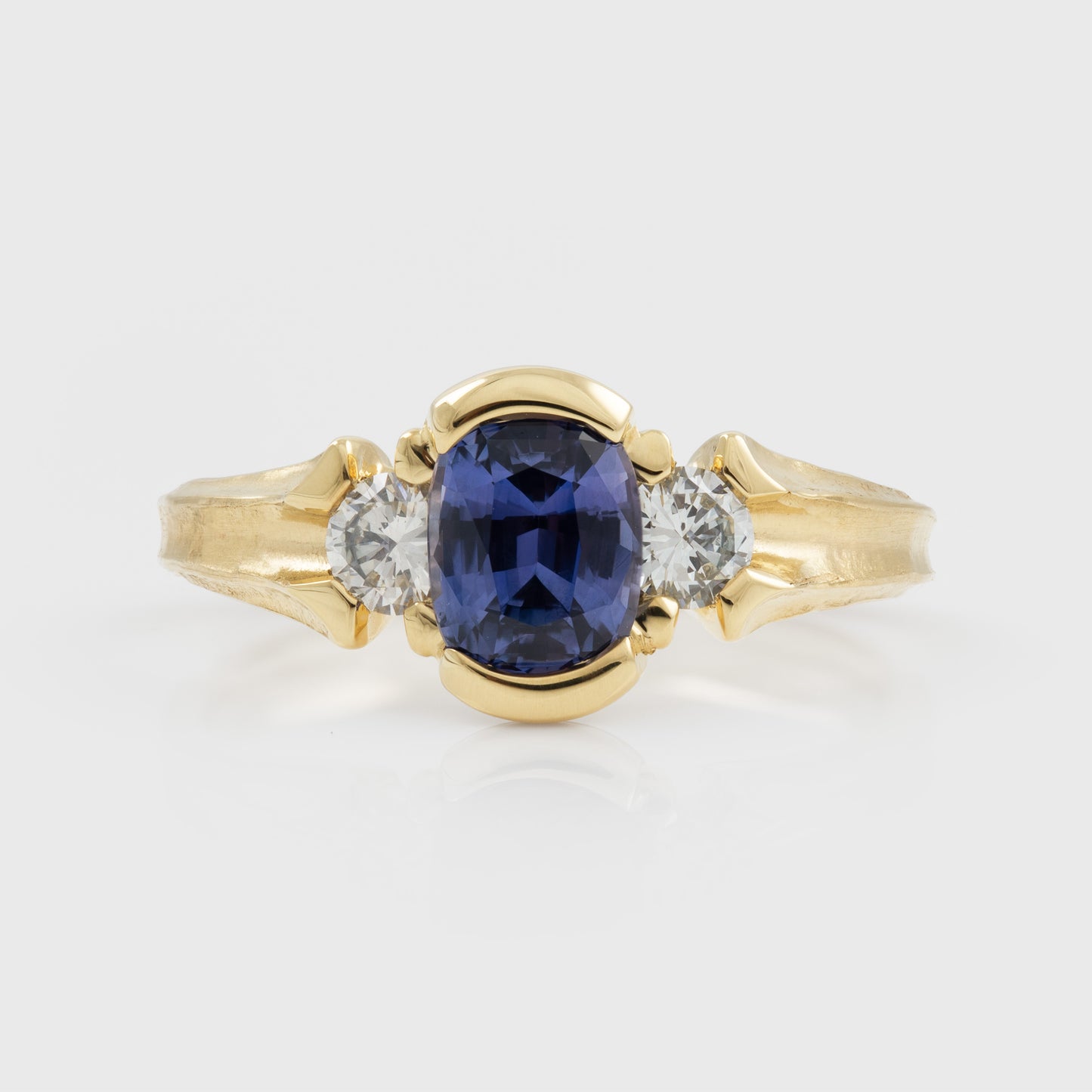 Yellow gold ring featuring half bezel set oval purple Sapphire flanked by round white Diamond accents