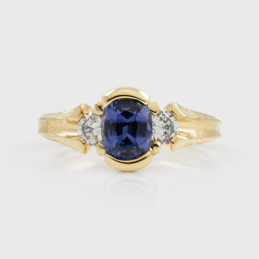 Yellow gold ring featuring half bezel set oval purple Sapphire flanked by round white Diamond accents
