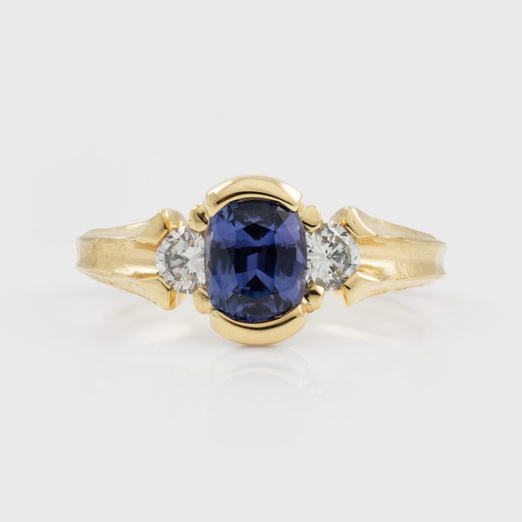 Yellow gold ring featuring half bezel set oval purple Sapphire flanked by round white Diamond accents