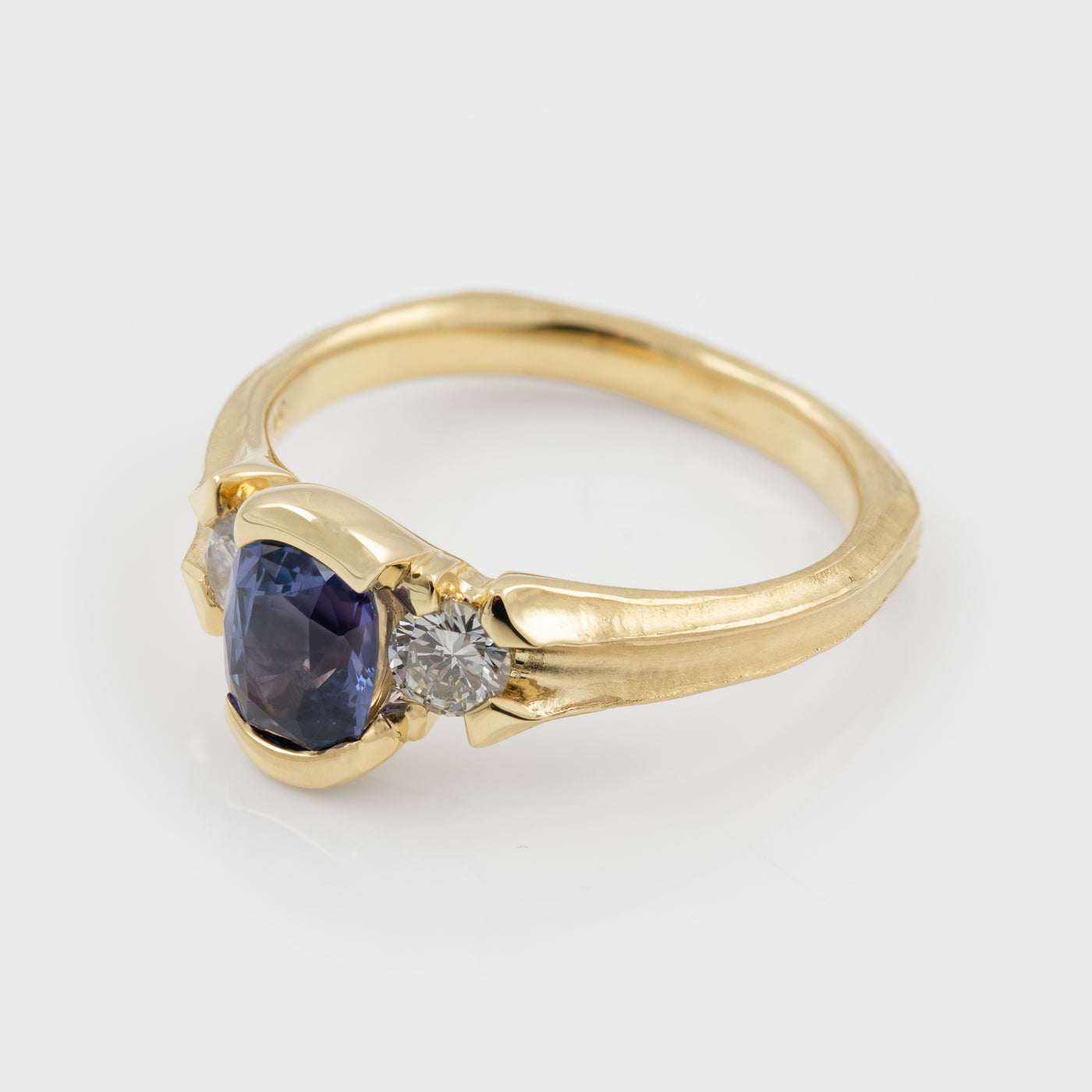 Side view of Yellow gold ring featuring half bezel set oval purple Sapphire flanked by round white Diamond accents