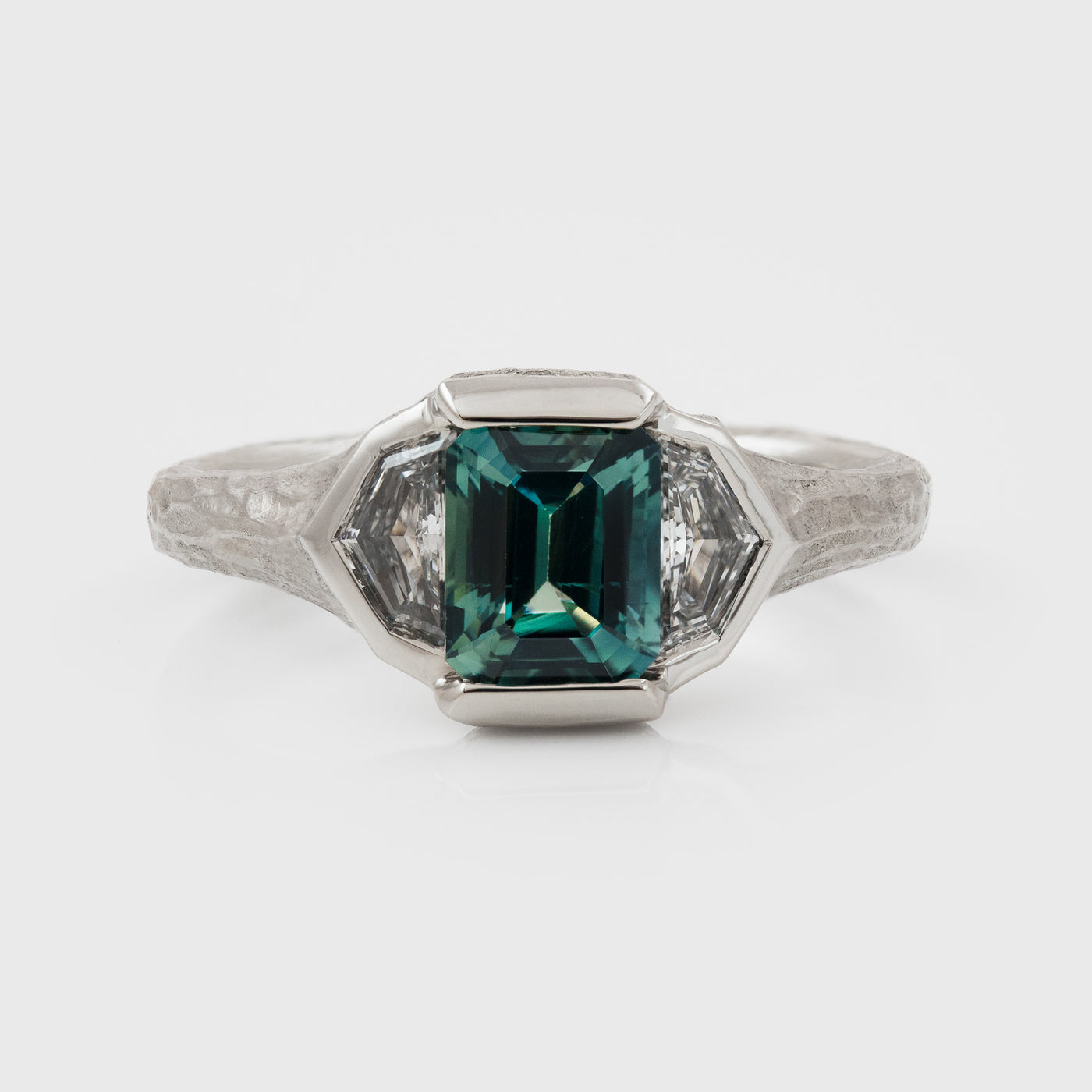 Platinum ring with green center gemstone and two accent diamonds on a white background