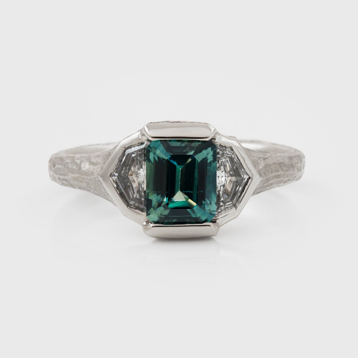 Platinum ring with green center gemstone and two accent diamonds on a white background