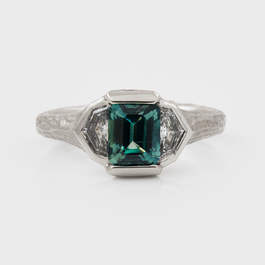 Platinum ring with green center gemstone and two accent diamonds on a white background