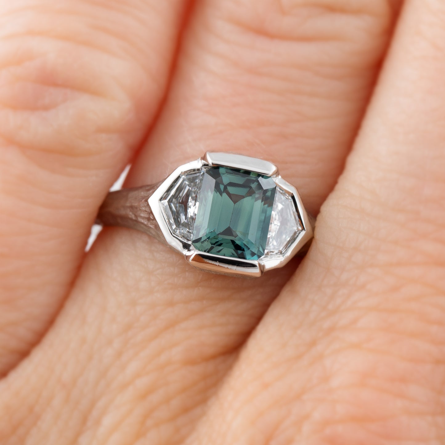 Platinum ring with green center gemstone and two accent diamonds on a hand