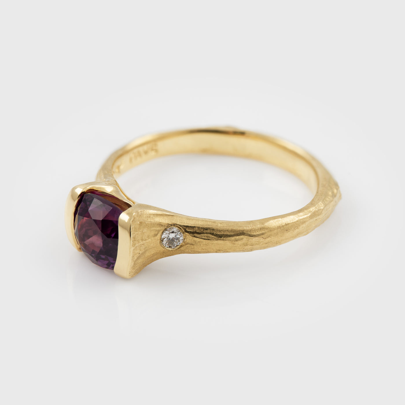 Gold ring with a purple gemstone and small diamond on a white background