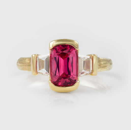 A yellow gold ring featuring a large rectangular pink gemstone in the center, flanked by two clear diamonds on a light gray background.