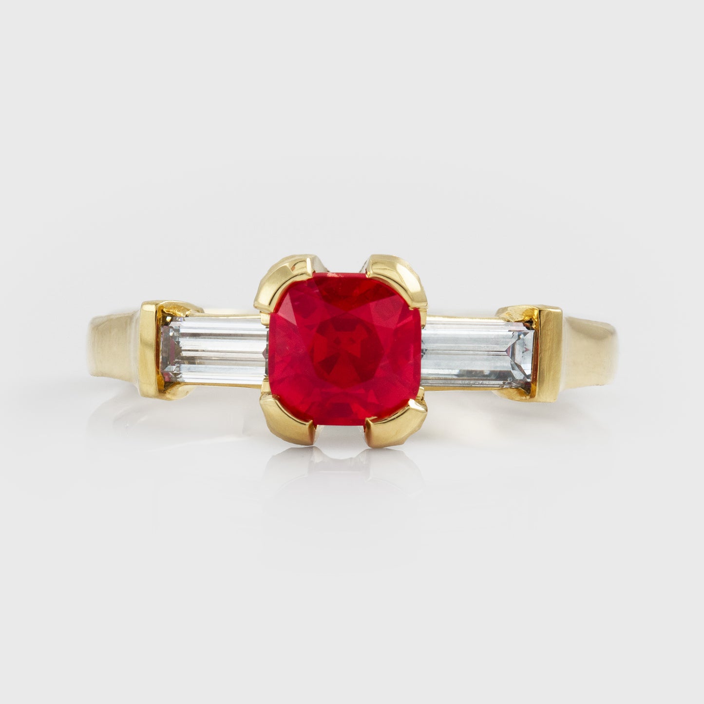 Yellow gold ring with red spinel center gemstone and two diamond accent stones on a white background