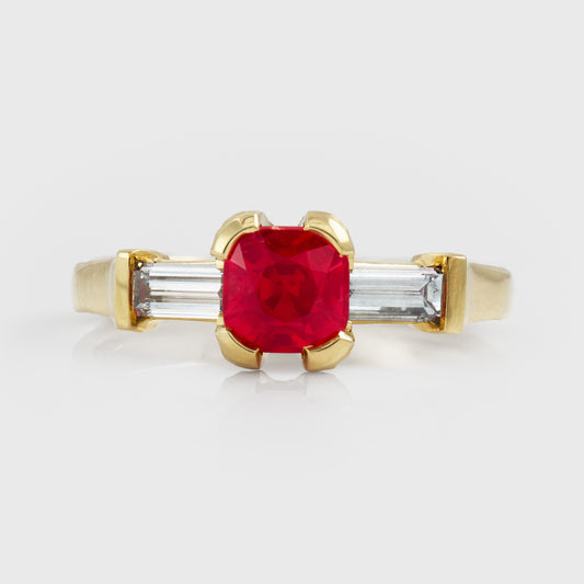 Yellow gold ring with red spinel center gemstone and two diamond accent stones on a white background
