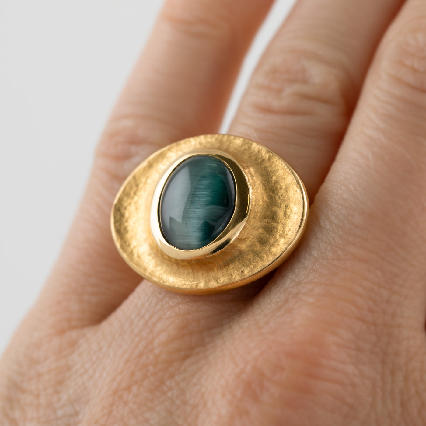 Yellow gold ring featuring bezel set blue green Cat's Eye Tourmaline worn on a hand