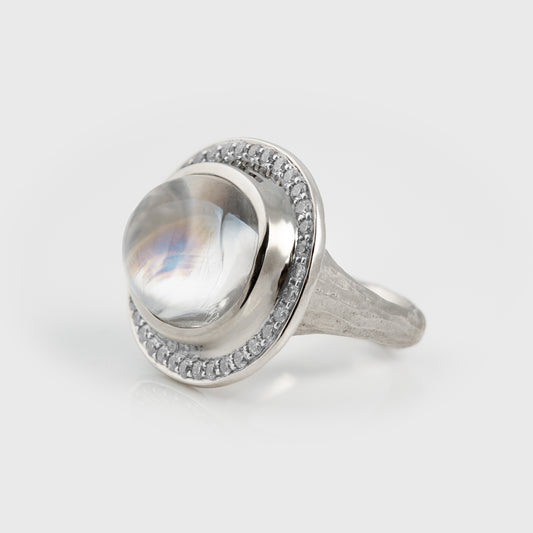Platinum ring featuring a large oval multicolor stone surrounded by diamonds and a textured band, photographed on a white background.

