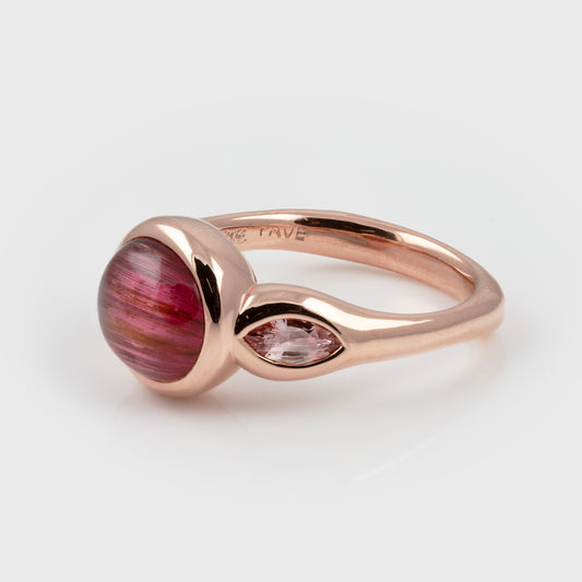 Side view of ring featuring a pink cat’s eye center stone accented by pink sapphire, photographed on a white background. Side band reads PAVE