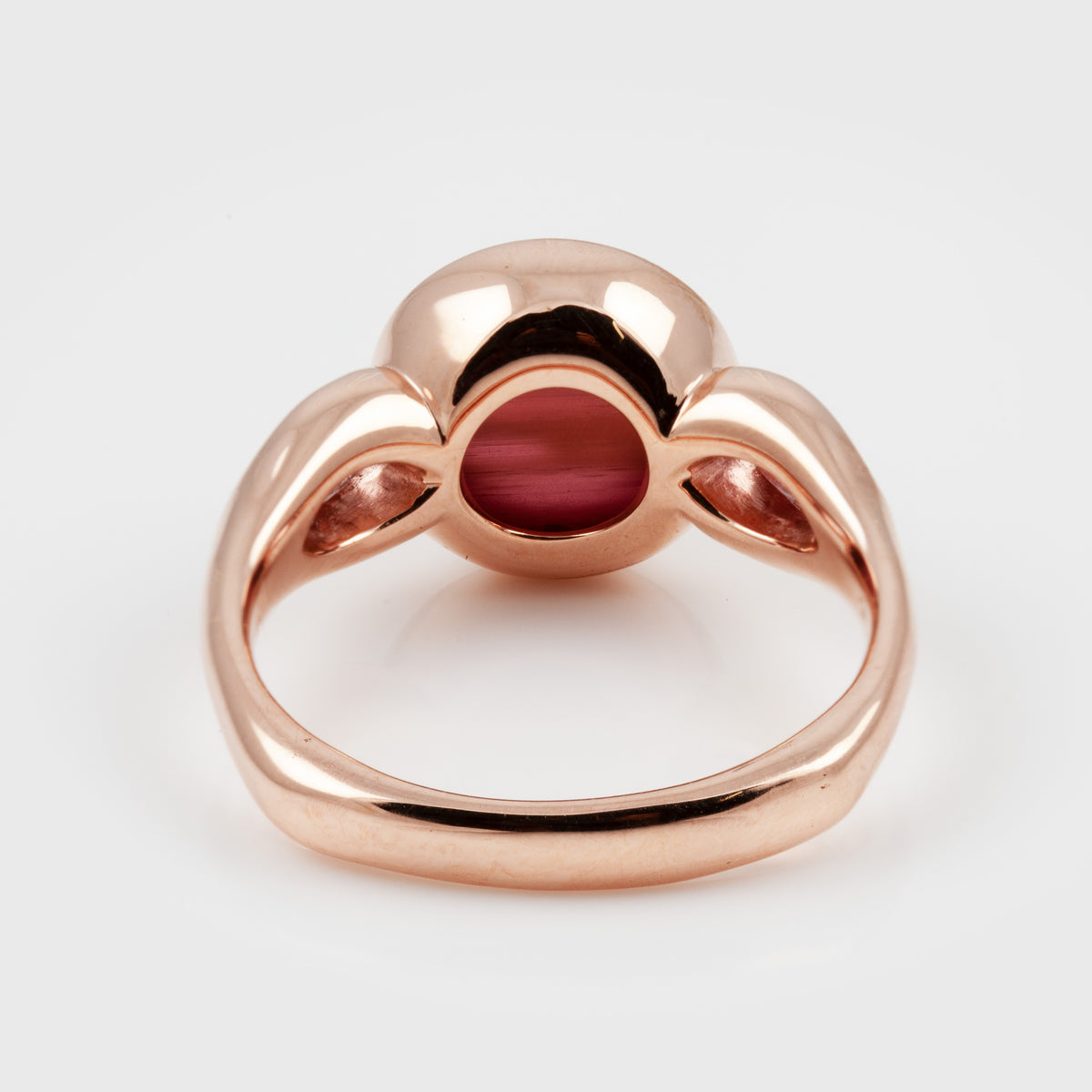 The back feature of a rose gold ring with a central oval red gemstone, photographed on a clean white background.