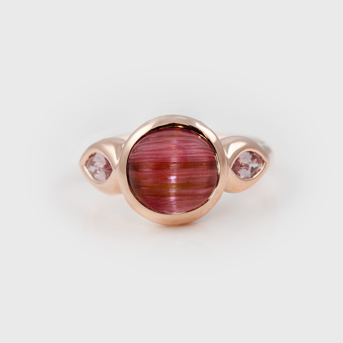 Ring featuring a pink cat’s eye center stone accented by pink sapphire, photographed on a white background.
